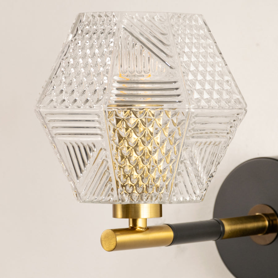 Closeup of gold metal wall light with geometric glass shade showcasing intricate pattern and premium finish for modern decor styling.