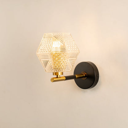 A black and gold wall light with a textured clear glass shade glowing on a beige background adding decorative sparkle and artistic modern décor.