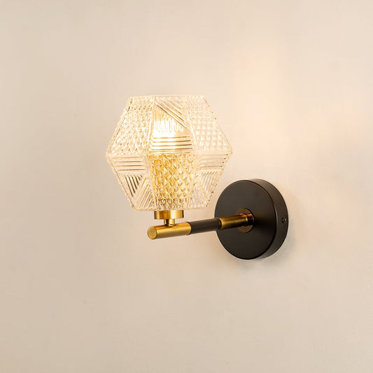 A black and gold wall light with a textured clear glass shade glowing on a beige background adding decorative sparkle and artistic modern décor.