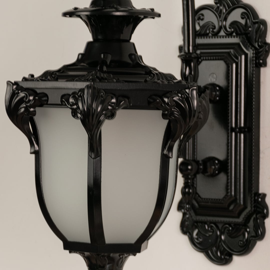 Close view of black metal lantern with detailed carving and frosted glass shade showing premium outdoor lighting design.