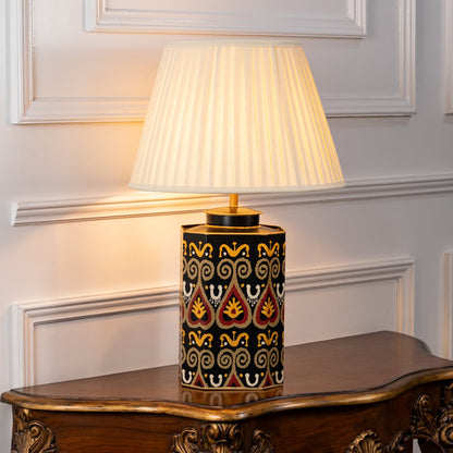 Designer table lamp with pleated white shade and black ceramic base highlighted by colorful traditional patterns and gold finish.