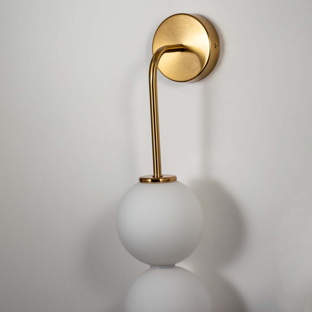 Modern wall light with gold finish and single white glass globe on neutral background minimal elegant lighting for bedroom decor.