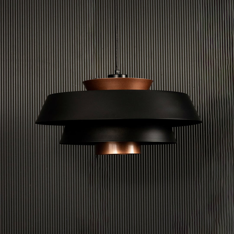 Modern black and copper pendant light displayed on dark background with lights off emphasizing its artistic layered finish.