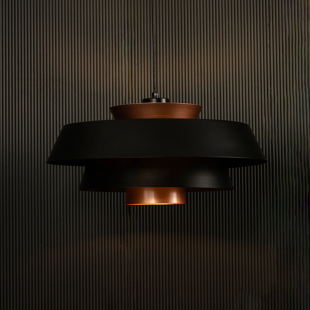 Elegant black and copper pendant light illuminated on dark background showcasing its unique layered industrial design style.