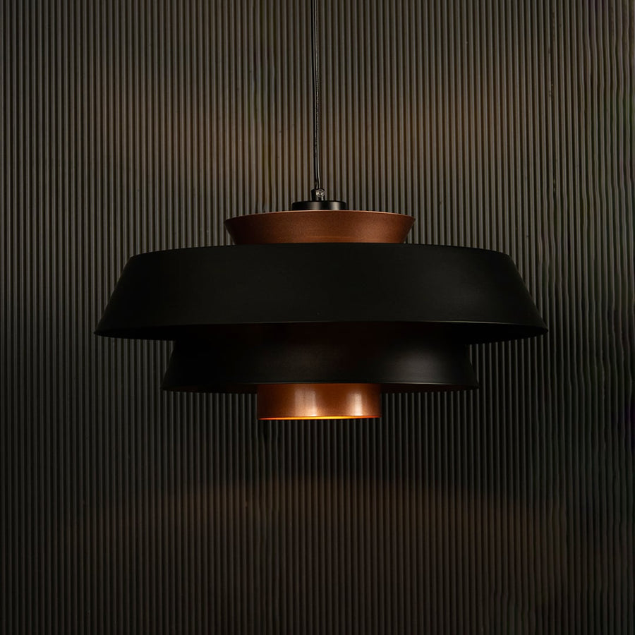 Elegant black and copper pendant light illuminated on dark background showcasing its unique layered industrial design style.