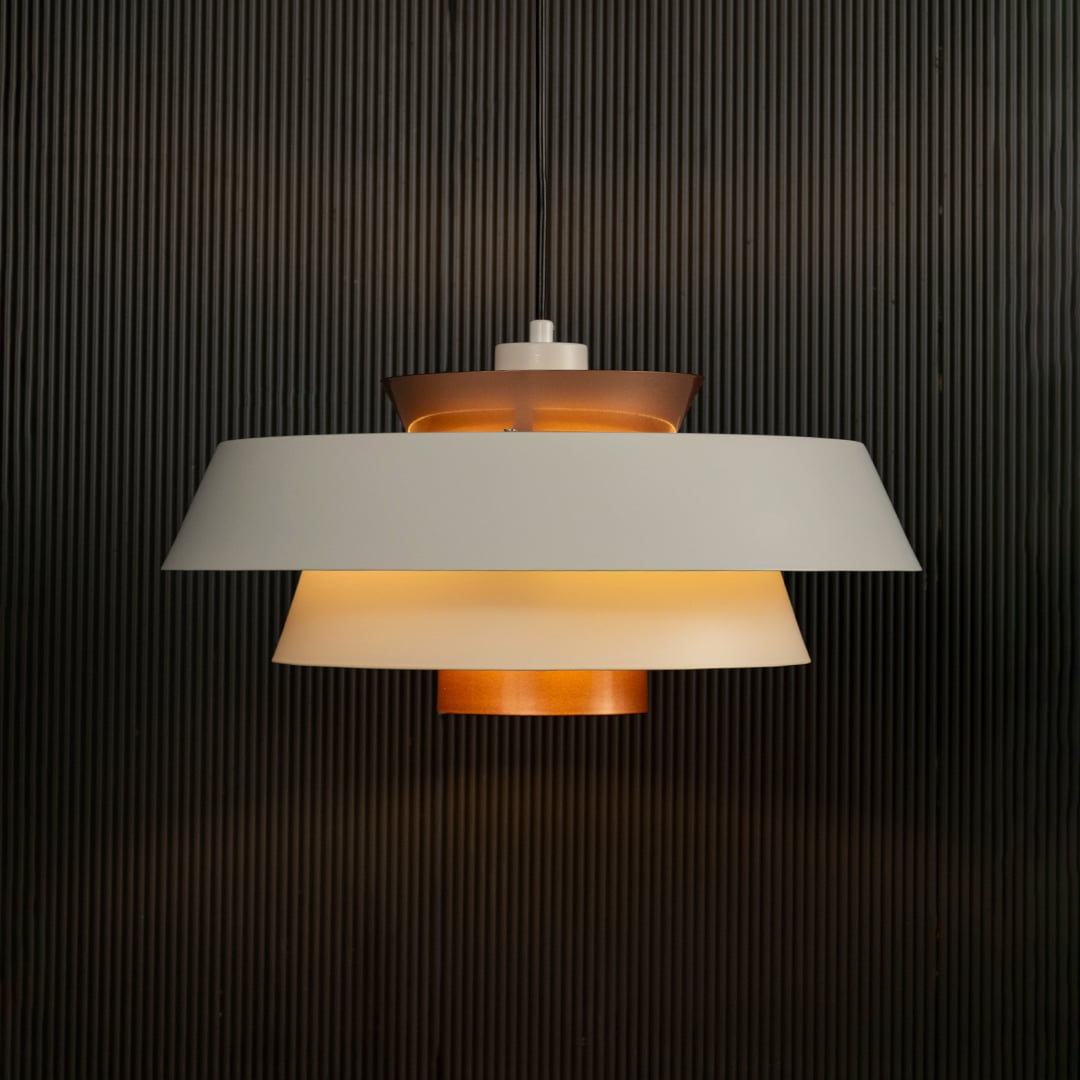 Elegant white and copper pendant hanging light illuminated against dark background highlighting its sleek layered modern industrial design.