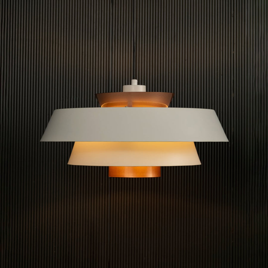 Elegant white and copper pendant hanging light illuminated against dark background highlighting its sleek layered modern industrial design.