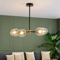 Modern three-light linear chandelier with clear glass bubble shades and gold accents, hanging in a living room with a green paneled wall and sofa.