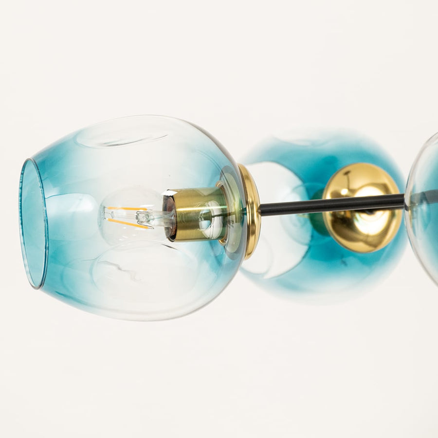 Closeup of blue tinted glass globe light with gold metal rod showing elegant transparency smooth finish and decorative lighting appeal.