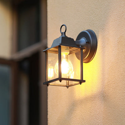 A compact black outdoor wall light glowing warmly on a textured wall creating a soft ambient light that enhances the exterior space during the evening.