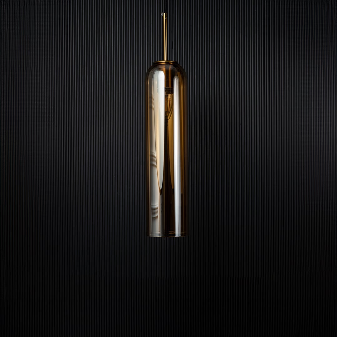 A cylindrical pendant light shown against a deep black background emphasizing its smooth reflective glass surface and modern silhouette with the light off.