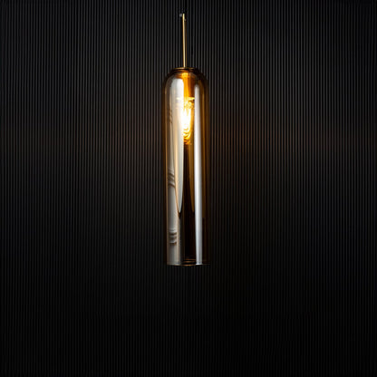 A glowing cylindrical pendant light illuminated against a dark backdrop creating a warm contrast that highlights the shape and reflective glass texture with the light on.
