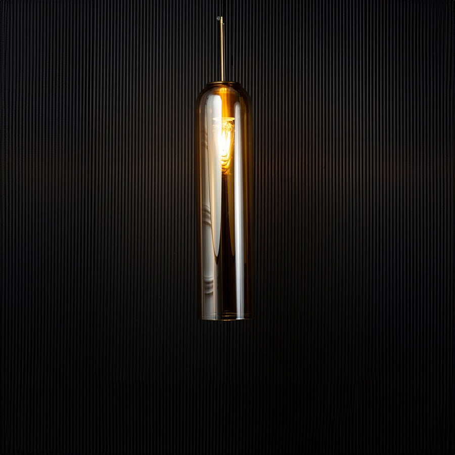 A glowing cylindrical pendant light illuminated against a dark backdrop creating a warm contrast that highlights the shape and reflective glass texture with the light on.