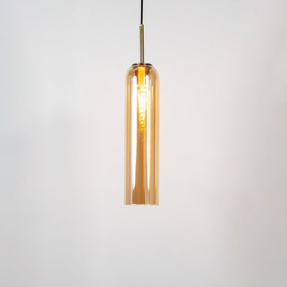 A tall cylindrical pendant light with its bulb glowing warmly on a white background showing its smooth transparent glass body and elegant metal detailing with the light on.