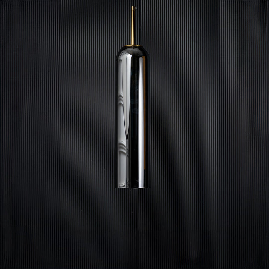 A tall silver cylindrical pendant light displayed on a black background with the light turned off emphasizing its glossy surface and slim elegant silhouette.