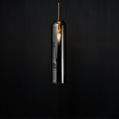 A modern silver cylindrical pendant light against a deep black background with the light turned on casting a warm glow and highlighting its reflective finish.