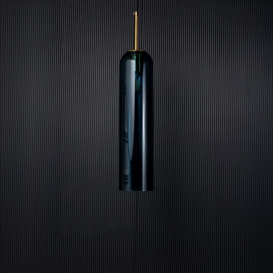 A blue glass pendant light turned off on a solid black background presenting its smooth cylindrical shape and rich blue tone with subtle gold features.