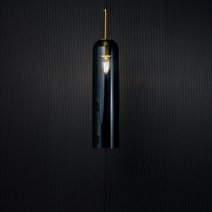 A glowing blue glass pendant light turned on against a deep black background creating a striking contrast that enhances its tall transparent design and warm radiance.