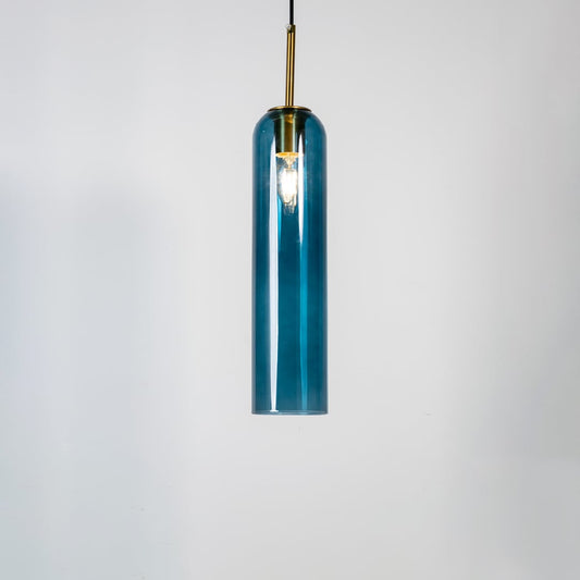 A blue glass pendant light turned on against a clean white background showcasing its glowing warm illumination and tall cylindrical design with gold detailing.