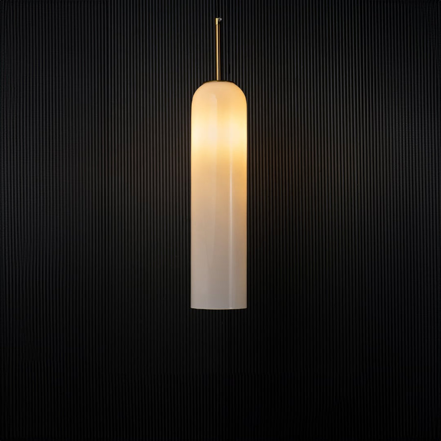 A modern cylindrical pendant light with the light on illuminating softly and creating a warm halo effect against a dark black background for dramatic contrast.