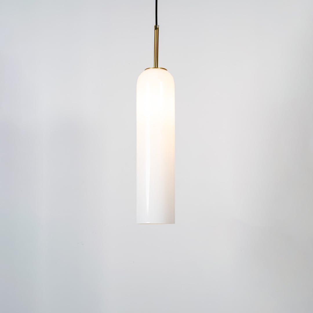 A tall cylindrical pendant light with the light on glowing warmly through the glass shade against a clean white background for a bright contemporary look.