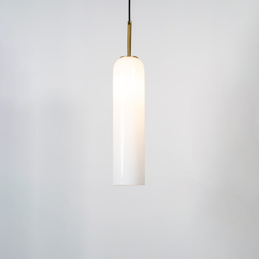 A tall cylindrical pendant light with the light on glowing warmly through the glass shade against a clean white background for a bright contemporary look.