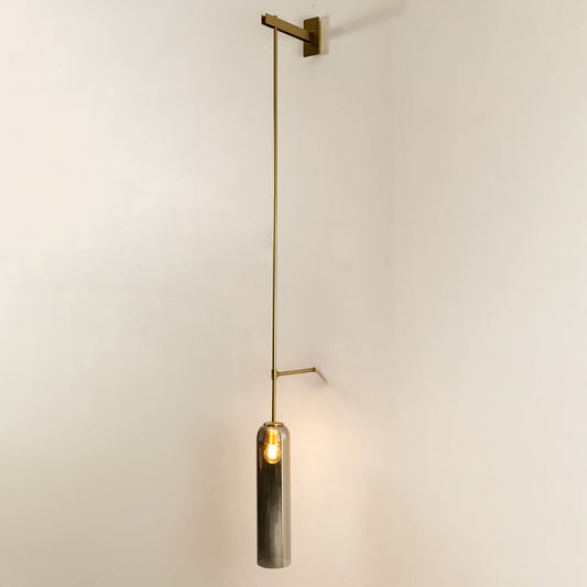 Wall pendant light with sleek metal arm and smoked glass cylinder glowing softly against a clean white background showcasing minimalist interior home decor lighting style.