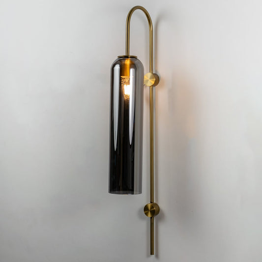 A tall glass wall light with metal frame shown with the light on against a clean white background highlighting its warm glow and modern structure.