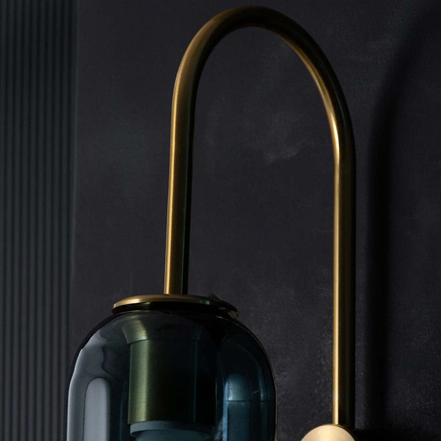 Detailed closeup of teal glass and gold wall light highlighting its tall cylinder shade and polished metal accents for luxurious contemporary decor.
