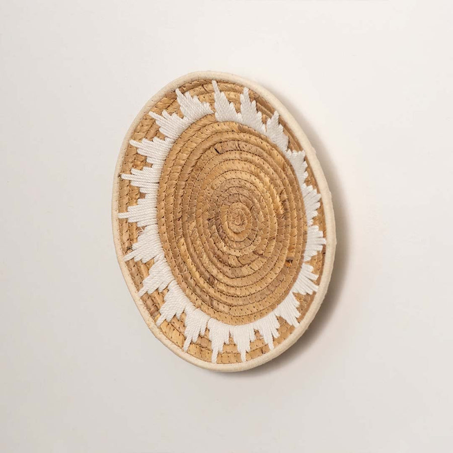 Side profile of the flat woven wall basket showing the thick natural fiber coils and white wrapping details on a white surface.