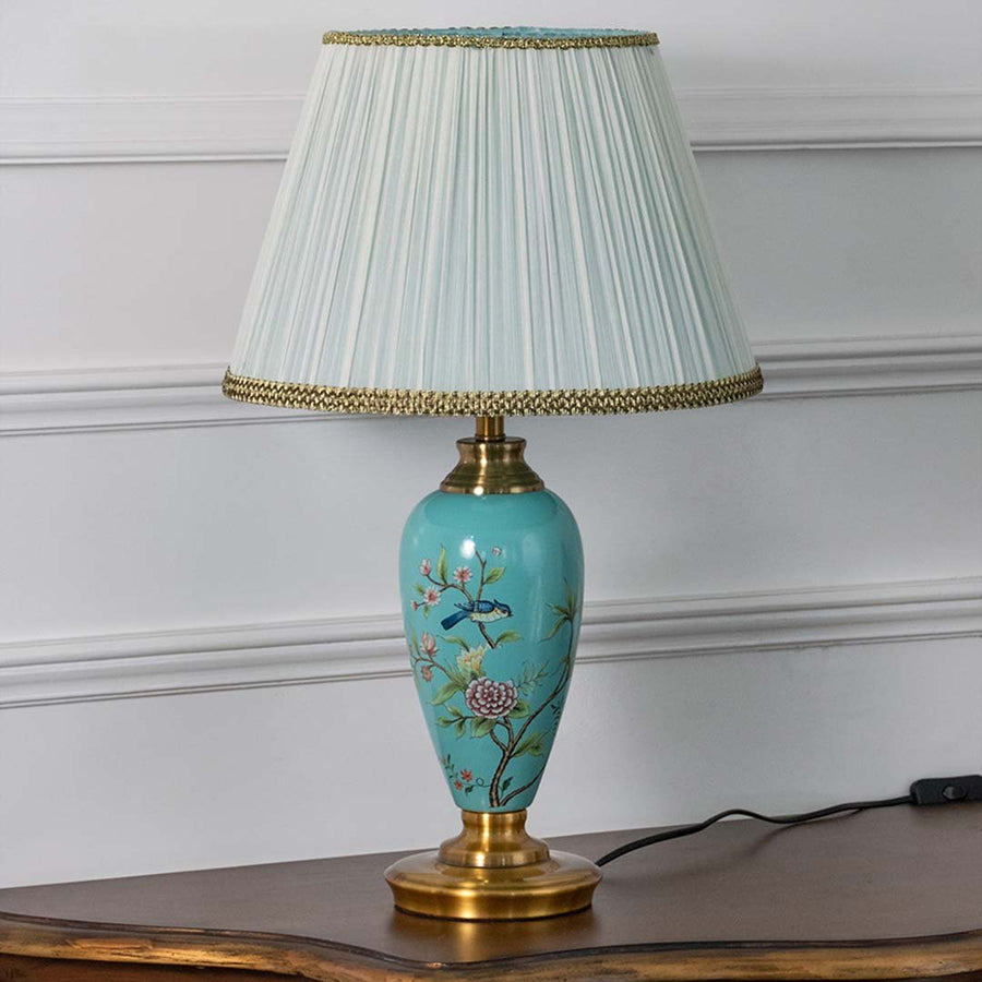 Turquoise floral ceramic table lamp with pleated fabric shade offering elegant traditional decor and ambient lighting indoors.