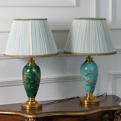 Emerald green ceramic table lamp featuring intricate gold leaf detailing and a pleated white shade turned off on a white background highlighting its glossy artistic finish.