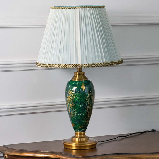 Emerald green ceramic table lamp featuring intricate gold leaf detailing and a pleated white shade turned off on a white background highlighting its glossy artistic finish.