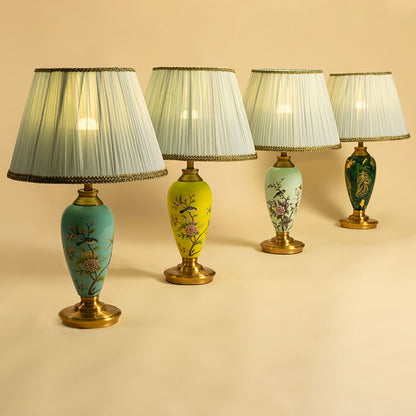 Collection of floral ceramic table lamps in mint green  turquoise  yellow  and emerald green with gold bases and pleated white shades turned on together spreading warm elegant illumination.