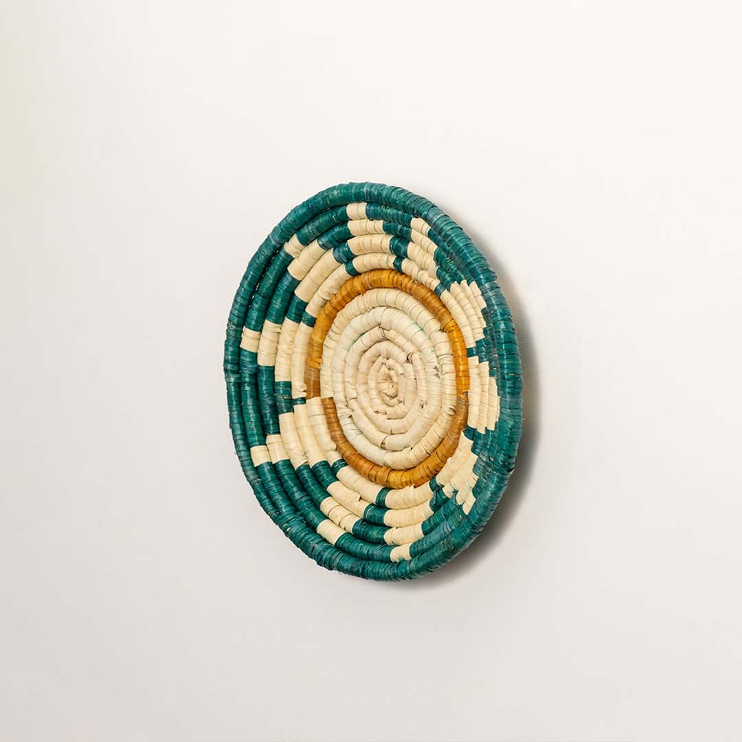 A side profile of the teal mustard and natural rattan wall decor plate showing its raised rim and detailed weaving for warm artisan inspired interior styling.