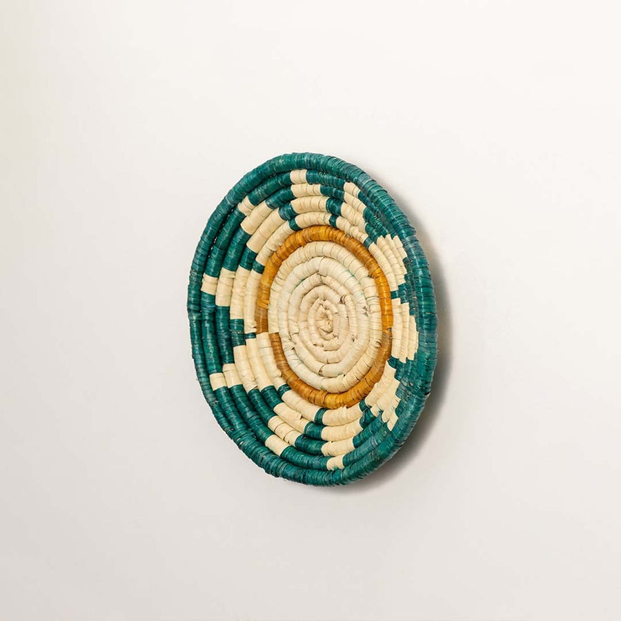 A side profile of the teal mustard and natural rattan wall decor plate showing its raised rim and detailed weaving for warm artisan inspired interior styling.