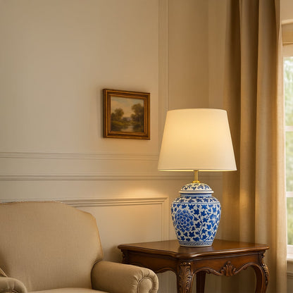 Elegant blue and white ceramic table lamp with warm light placed on a carved wooden side table in a classic living room setting.