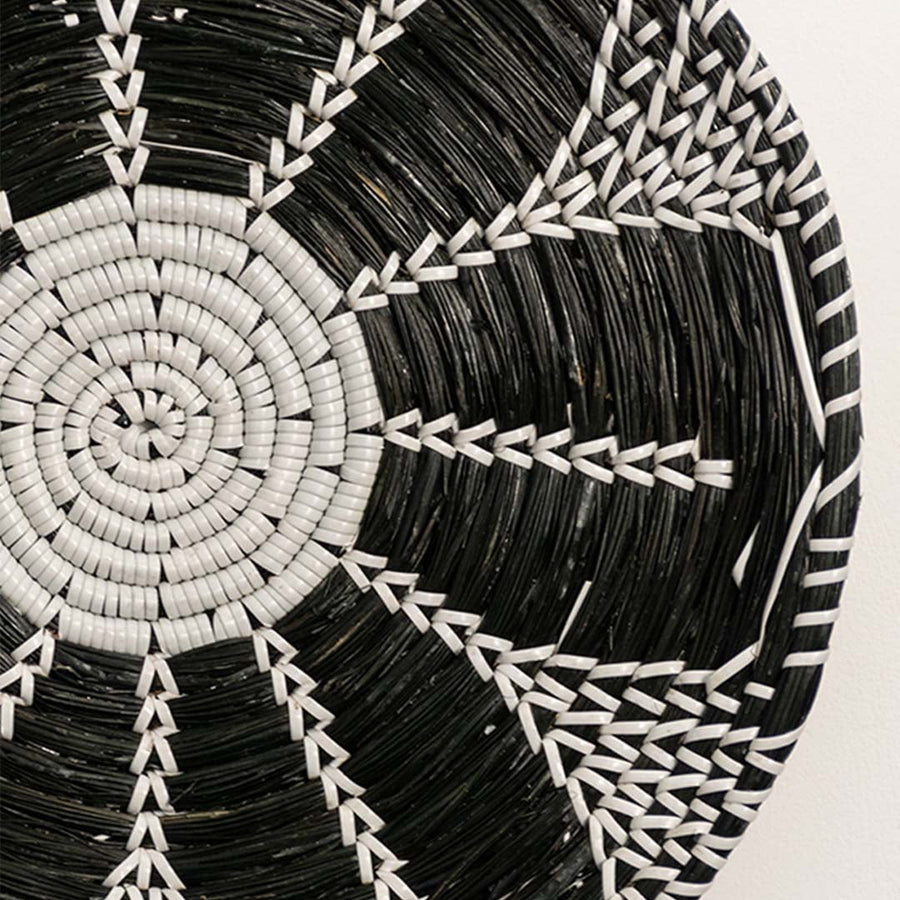 Detailed closeup view of the tight weaving and painted black and white sections on the natural seagrass wall basket surface quality.