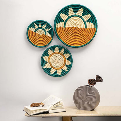 A grouped arrangement of teal mustard and natural rattan wall decor plates on a white wall above a marble table with an open book creating a warm handcrafted home styling look.