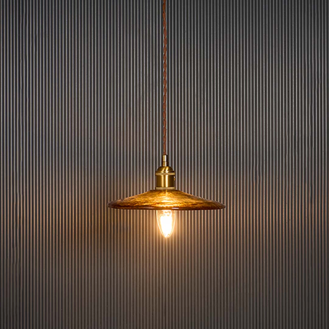 Elegant brass pendant light illuminated against a black background showing warm glow through the metal shade ideal for vintage interiors.