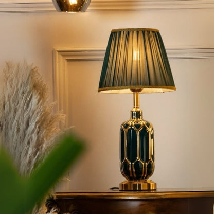 Elegant table lamp with a patterned emerald ceramic base gold accents and a pleated green shade placed on a wooden table in a warm cozy interior.