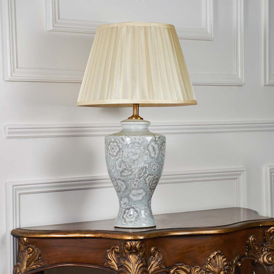 Ceramic table lamp with floral patterns and pleated shade shown on a white backdrop emphasizing its sculpted silhouette and craftsmanship.