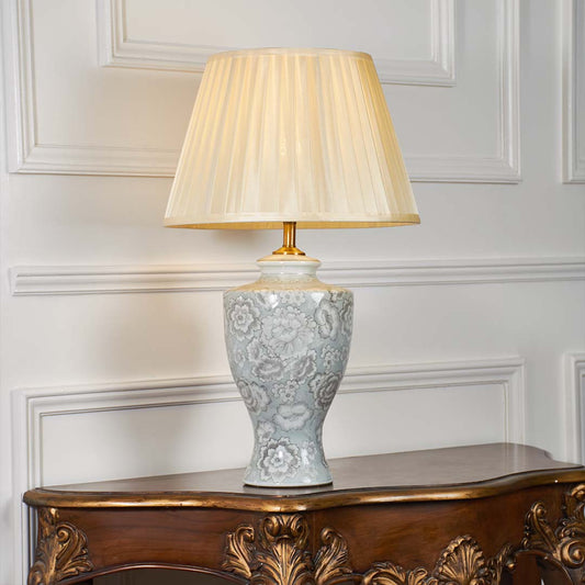 Grey floral ceramic table lamp with pleated shade displayed on a clean white background highlighting its intricate textured detailing.