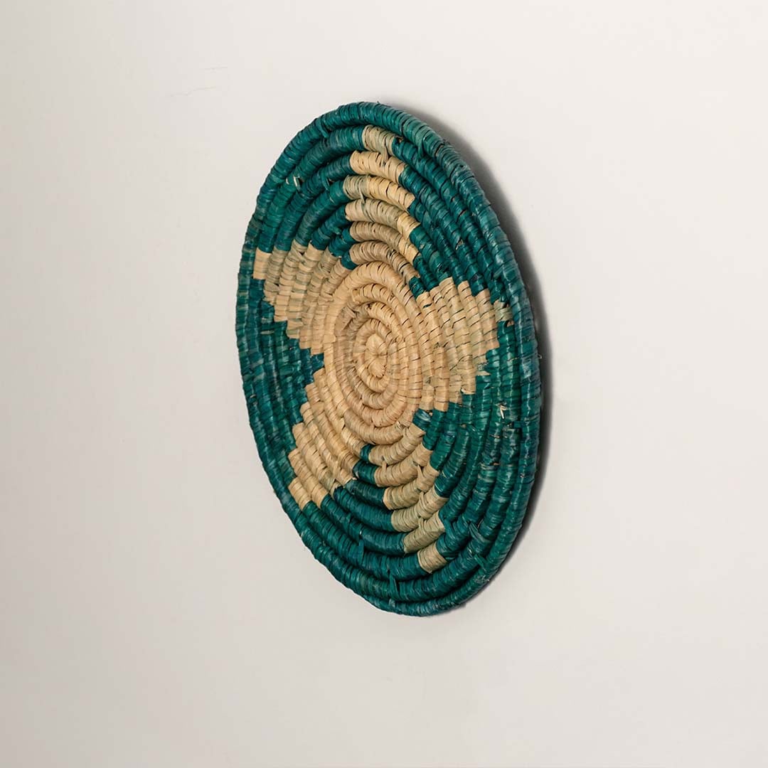 Side profile of the flat woven wall basket showing the thick natural fiber coils and teal stitching details on a white surface.