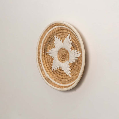 Side profile of the flat woven wall basket showing the thick natural fiber coils and white wrapping details on a white surface.
