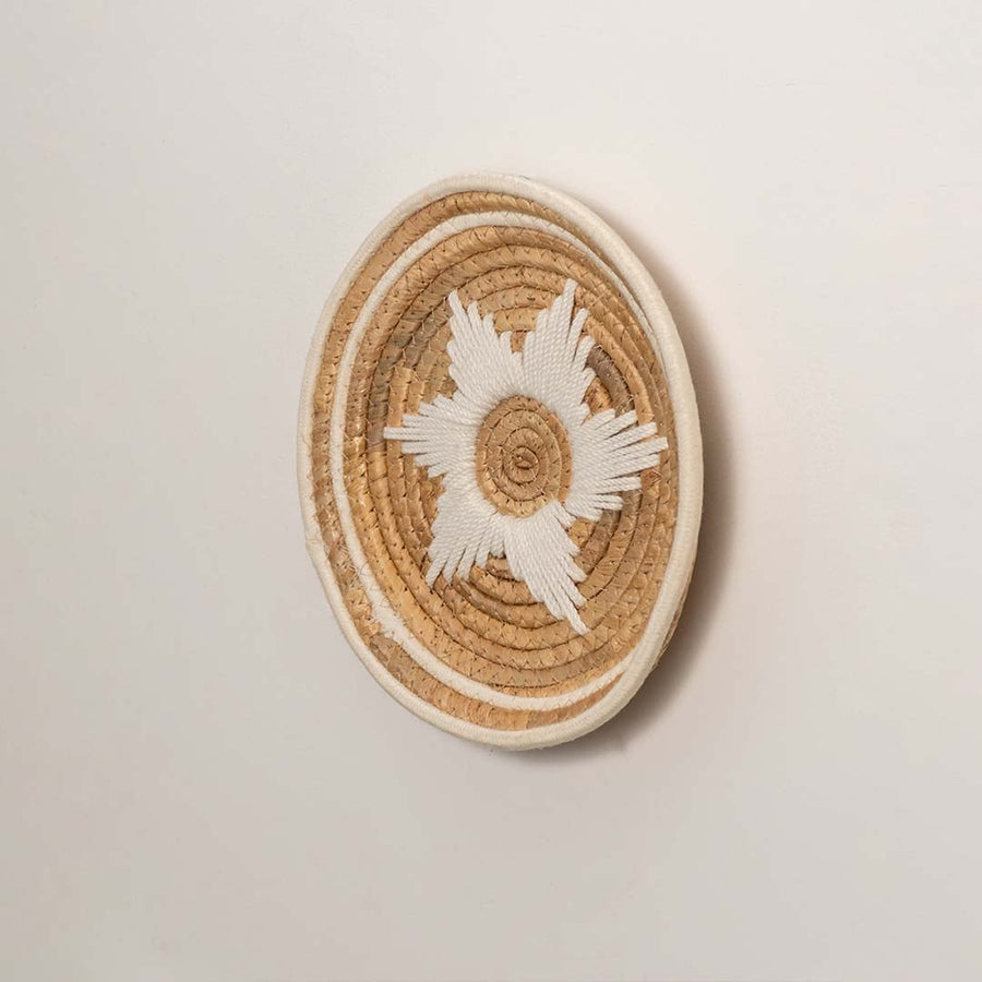 Side profile of the flat woven wall basket showing the thick natural fiber coils and white wrapping details on a white surface.