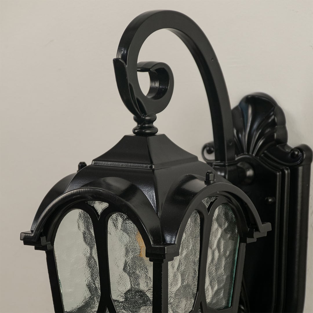 Closeup of the black outdoor lantern showing detailed curved metalwork and textured glass panels.