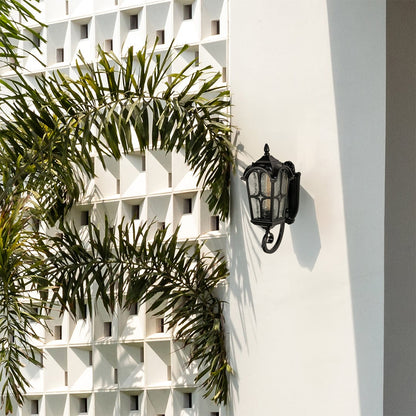Elegant black outdoor lantern mounted on a wall featuring curved metalwork and textured glass panels.