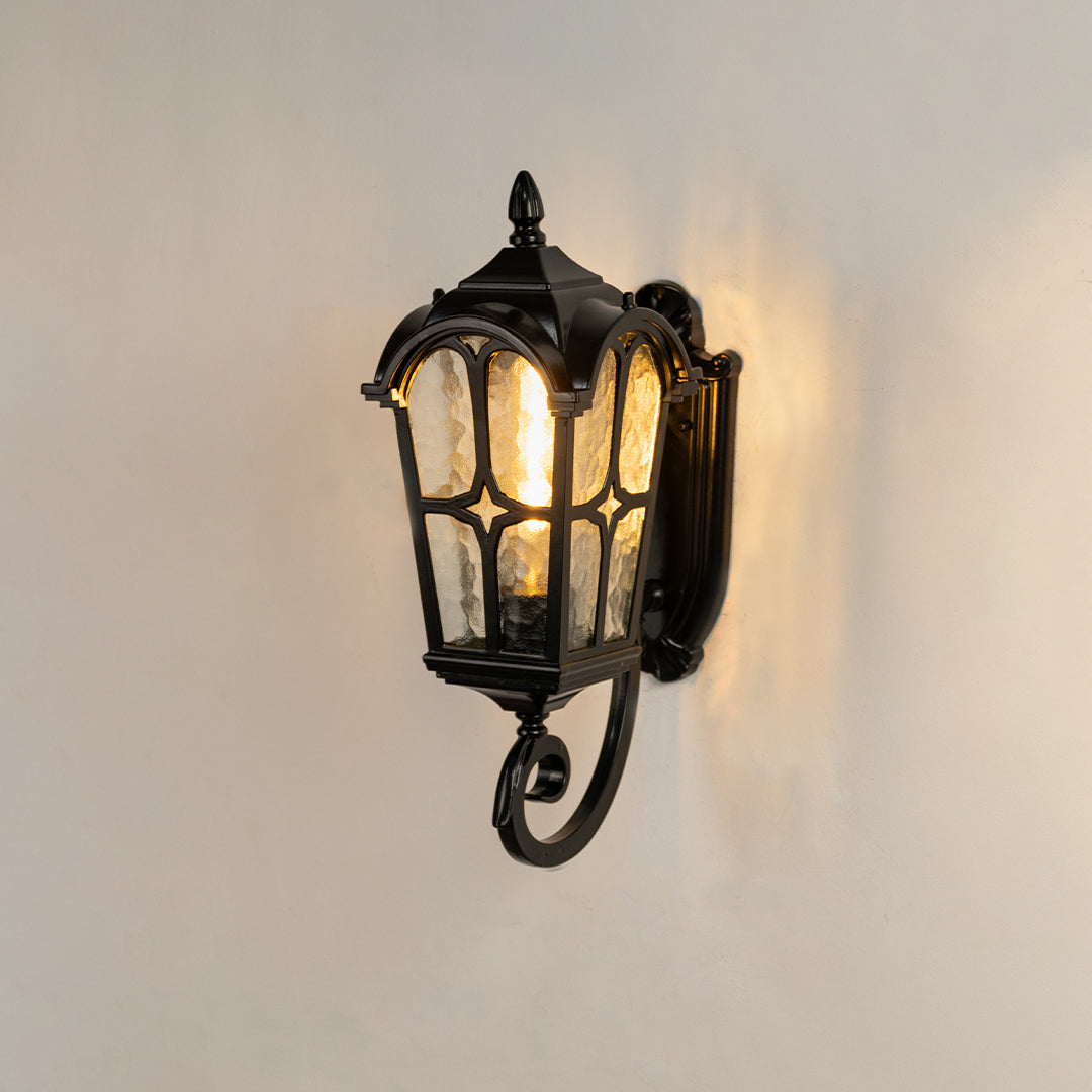 Classic black outdoor wall lantern on white background featuring textured water glass shade and an elegant bottom scroll arm.