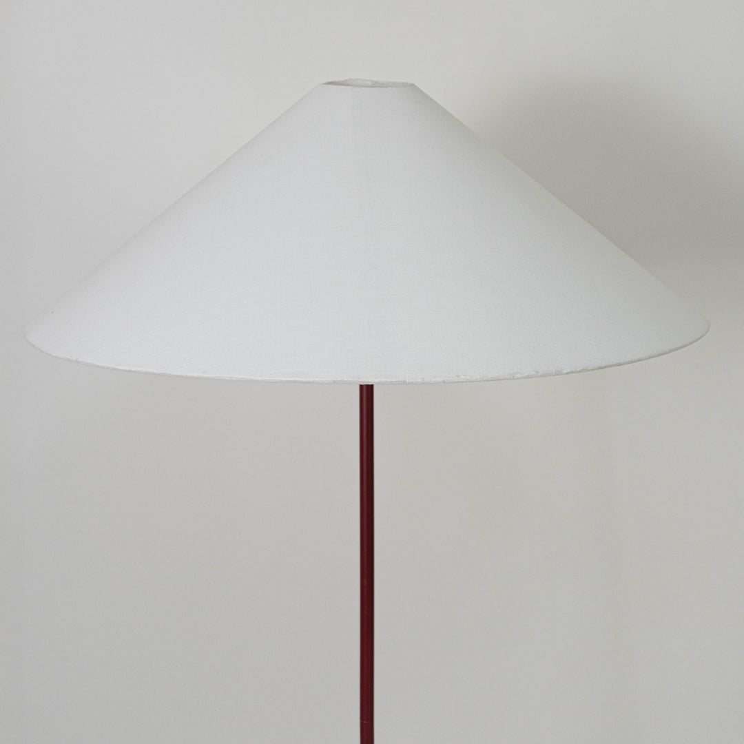 Large white conical lampshade supported by slim maroon rod designed to diffuse warm ambient light elegantly.